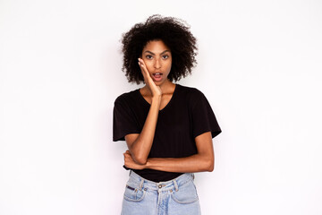 Fototapeta na wymiar Portrait of amazed young woman looking at camera with open mouth against white background. African American lady wearing black T-shirt and jeans expressing awe or surprise. Astonishment concept