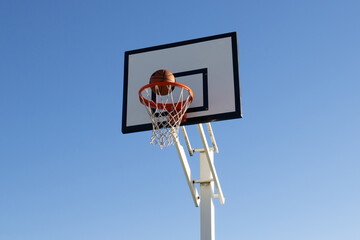 Low angle shot of orange basketball flying into hoop outside on sunny day. Ball thrown into basket...