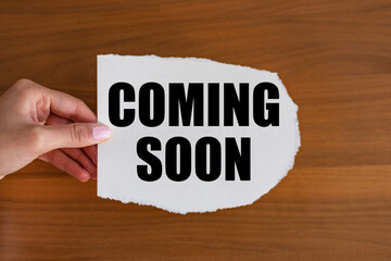 Coming soon. Woman hand holds a piece of paper with text. Information sign, opening event, business and premiere event.