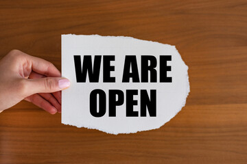 We are open - close up text on the slip. Woman hand holds a piece of paper with text. Opening event, reopening, business and marketing.