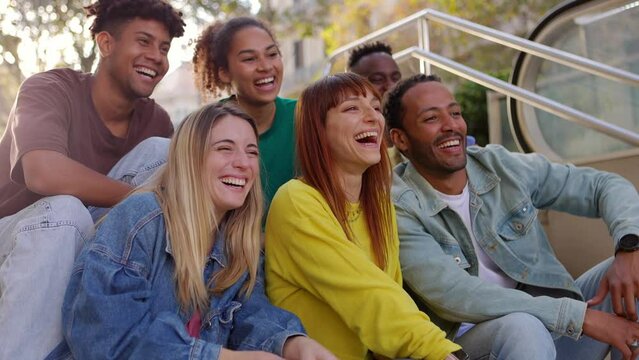 Young group of hispanic latin friends having fun together outdoors. Millennial multiracial people laughing while social gathering sitting on stairs at city street