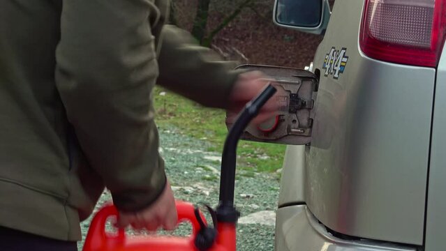 A man pouring gasoline into fuel tank from a plastic red gas can. Offroad fuel reserve.