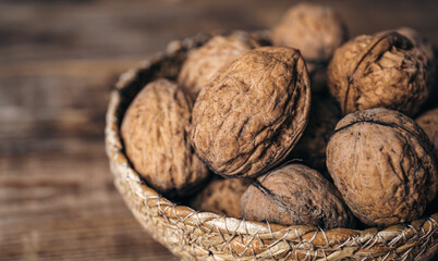 Close-up, whole walnuts in a wicker bowl on a wooden background.