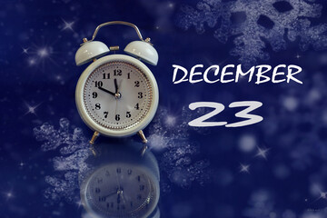 Calendar for December 23: white alarm clock on a blue background with bokeh, reflection from...