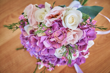 The bride's bouquet consists of white roses and pink hydrangeas, wedding rings on the bouquet. Close-up.