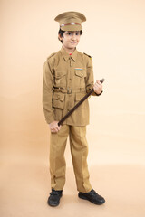 Young elementary indian boy kid wearing police uniform showing with his nightstick in hand isolated on beige studio background. Full length shot, career and dreams.