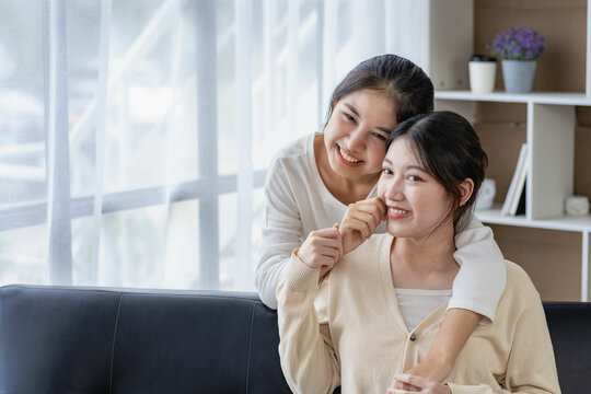 Young beautiful Asian LGBT lesbian happy couple sitting on sofa using smartphone in living room at home. LGBT lesbian couple living together