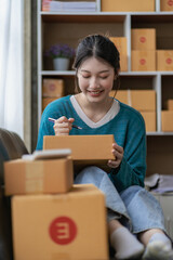 delivery concept SME, freelance Asian woman smiling using laptop computer with joyful success of boxed items, online marketing, selling at home.