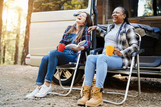 Multiracial women friends having fun camping with camper van while drinking coffee outdoor - Travel and friendship concept - Focus on african female face
