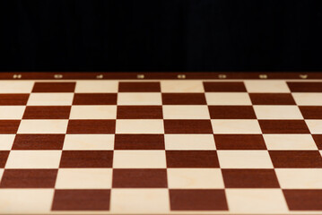 Empty wooden chessboard on a black background.
