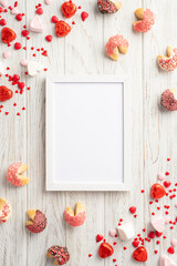Valentine's Day concept. Top view vertical photo of photo frame cookies and heart shaped candies on white wooden desk background with empty space