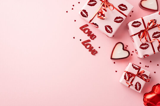 Valentine's Day concept. Top view photo of gift boxes in wrapping paper with kiss lips pattern heart shaped candles balloon confetti inscriptions love on isolated pastel pink background with copyspace