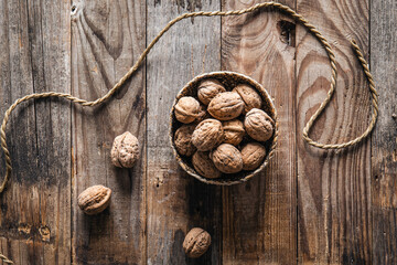 Bowl with whole walnuts on wooden background, flat lay.