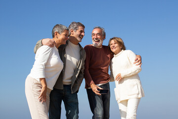 Two senior couples having fun outdoors on sunny day, standing against blue sky and laughing. Happy...