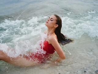 Woman lying on the ocean on the beach in the waves in a red swimsuit, a hotel vacation