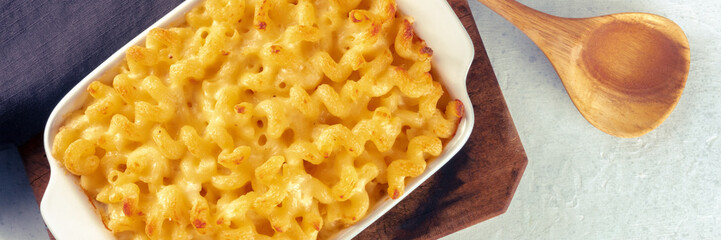Macaroni and cheese pasta in a casserole panorama, top shot with a wooden spoon. Cheesy American...