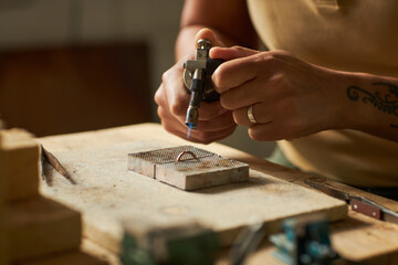 Close up of artisan jeweler welding ring at rustic workstation while creating handmade jewelry...