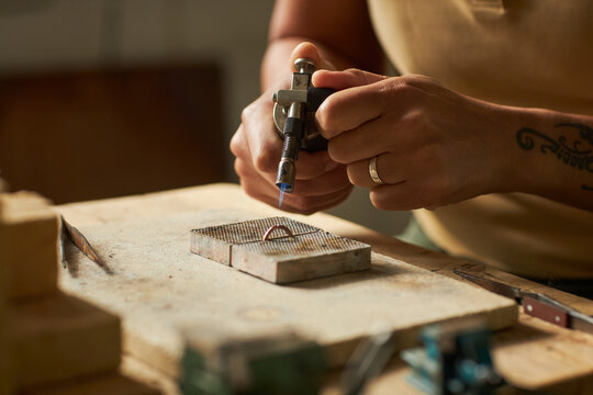 Close up of artisan jeweler welding ring at rustic workstation while creating handmade jewelry pieces, copy space