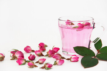 pink tea made from dried small rosebuds in a transparent mug on a white background