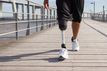 Close-up of man with mechanical leg walking on summer day. Sportsman in black shorts and white...