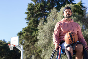 Bearded middle-aged man with prosthesis in wheelchair with basketball on his lap. Strong handsome...