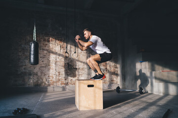 Strong sportsman jumping on wooden box in gym