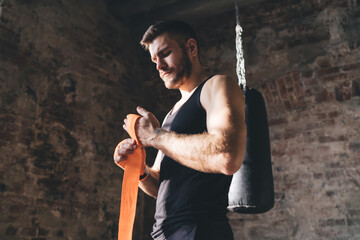 Serious sportsman wrapping hand with tape in gym