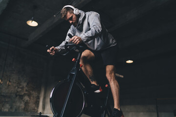 Man in headphones exercising on spinning cycle in gym