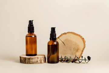 Two cosmetic bottles with face oil, serum or essential on wooden podium with eucalyptus leaves,...