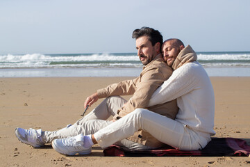 Affectionate man snuggling up boyfriend on beach. Calm bald gay hugging boyfriend at sea. LGBT concept