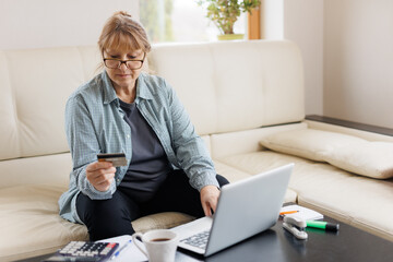 Happy mature woman grandmother using credit card , doing online shopping on laptop, buying new clothes, presents, paying domestic bills, pension at home	
