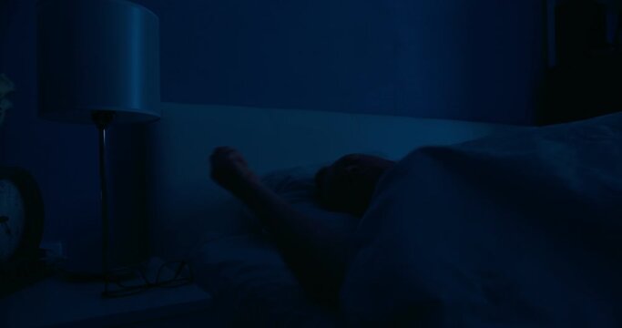 Man lays down in bed and turns off night light stand besides bed. medium shot