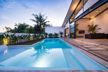 Tropical villa view with garden, swimming pool and open living room at sunset - obrazy, fototapety, plakaty