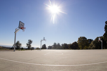 Empty sunlit basketball court in city park on hot sunny day under blue zenith sky. Bright sun in...