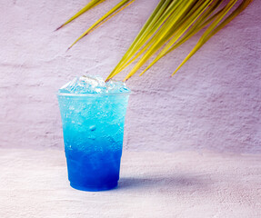 Blue Hawaiian drink in a plastic glass and coconut leaves.