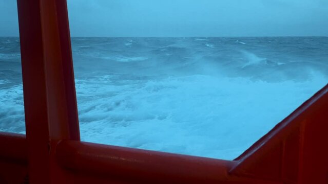 Board ship in storm. Strong wind breaks wave. Red side of vessel and green sea.