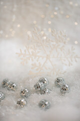 Christmas snowflake and small mirror balls on a snow. Blurred background with beautiful bokeh. Shallow depth of field. Copy space. Airy atmosphere. Soft focus. 