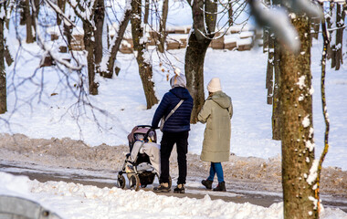 A married couple rolls a child in a wheelchair in the winter Park
