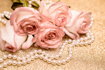 Pink rose and pearl necklace on a shiny gold background
