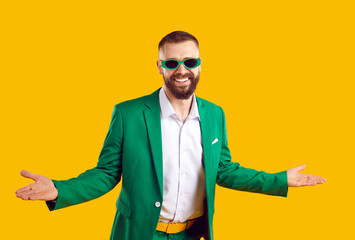 Funny happy bearded man wearing green suit and sun glasses standing isolated on yellow background,...