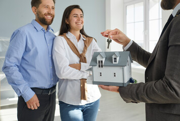 Realtor gives the key to a happy, smiling family. Real estate agent holding a toy house model and...