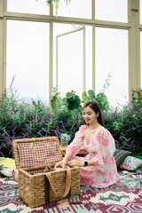 a beautiful woman was opening a wooden basket, full of foods for the picnic placed on a mat in the garden