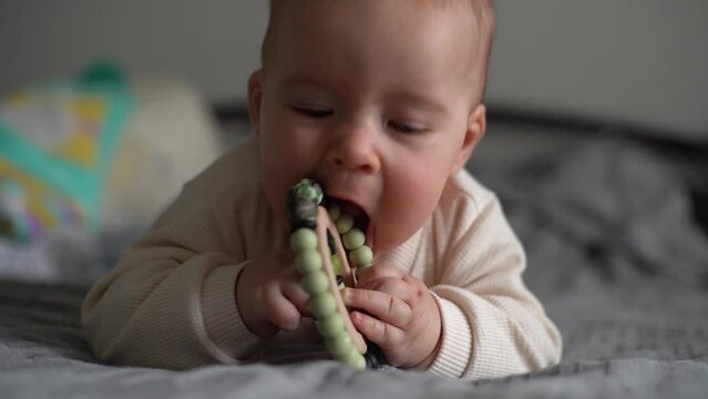 baby chewing teether toy. Infant growing first tooth. Boy biting toy on parents bed. Pretty six-month old baby boy. Realistic toddler home portrait