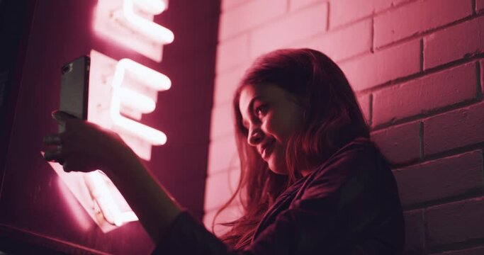 Phone selfie, night and woman with neon sign, creative shadow lighting and mobile cellphone for aesthetic picture. Pink light, creativity and beauty girl post night life memory to social network app