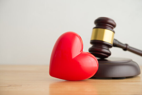 Red heart with hammer judge gavel on wooden office table and white wall background copy space. Family life issues, legal separation and divorce, legal marriage, love court law concept.