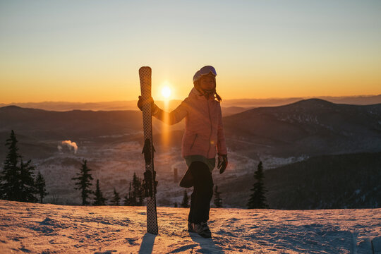 Silhouette of Skier female holding ski standing on mountain top during sunset, beautiful winter mountains landscape