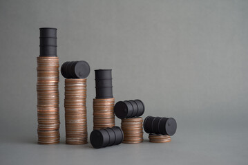 Crude oil tank on stack coins as price chart graph falling down on grey background copy space. World petroleum and energy industry or trading, crude oil level of price cap, revenue reduce concept.