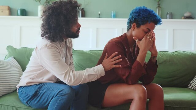 Young offended African American woman crying listening to apologies and requests for forgiveness Indian man after family fight or toxic relationship sits on sofa in living room. Multiracial people