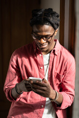 Smiling happy African American man standing indoors rejoicing reading positive comments from subscribers of own blog. Optimistic cheerful black guy influencer gets joyful emotions using smartphone