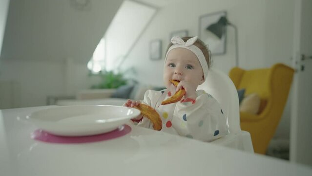 Slow motion - Cute little 8 month old baby girl sitting at a table and eating baked potato. Baby led weaning concept video